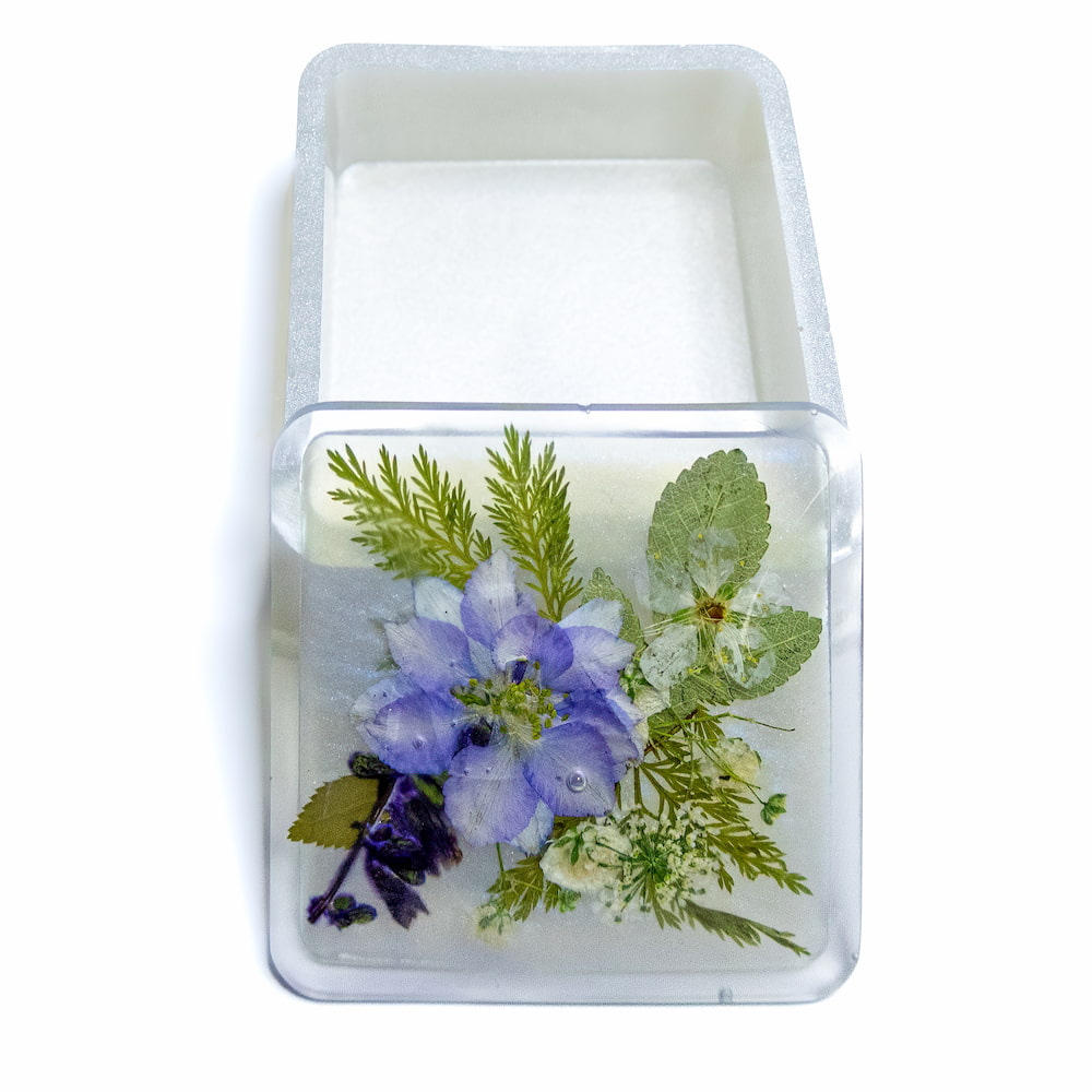 Square resin trinket container with pressed flowers on lid.